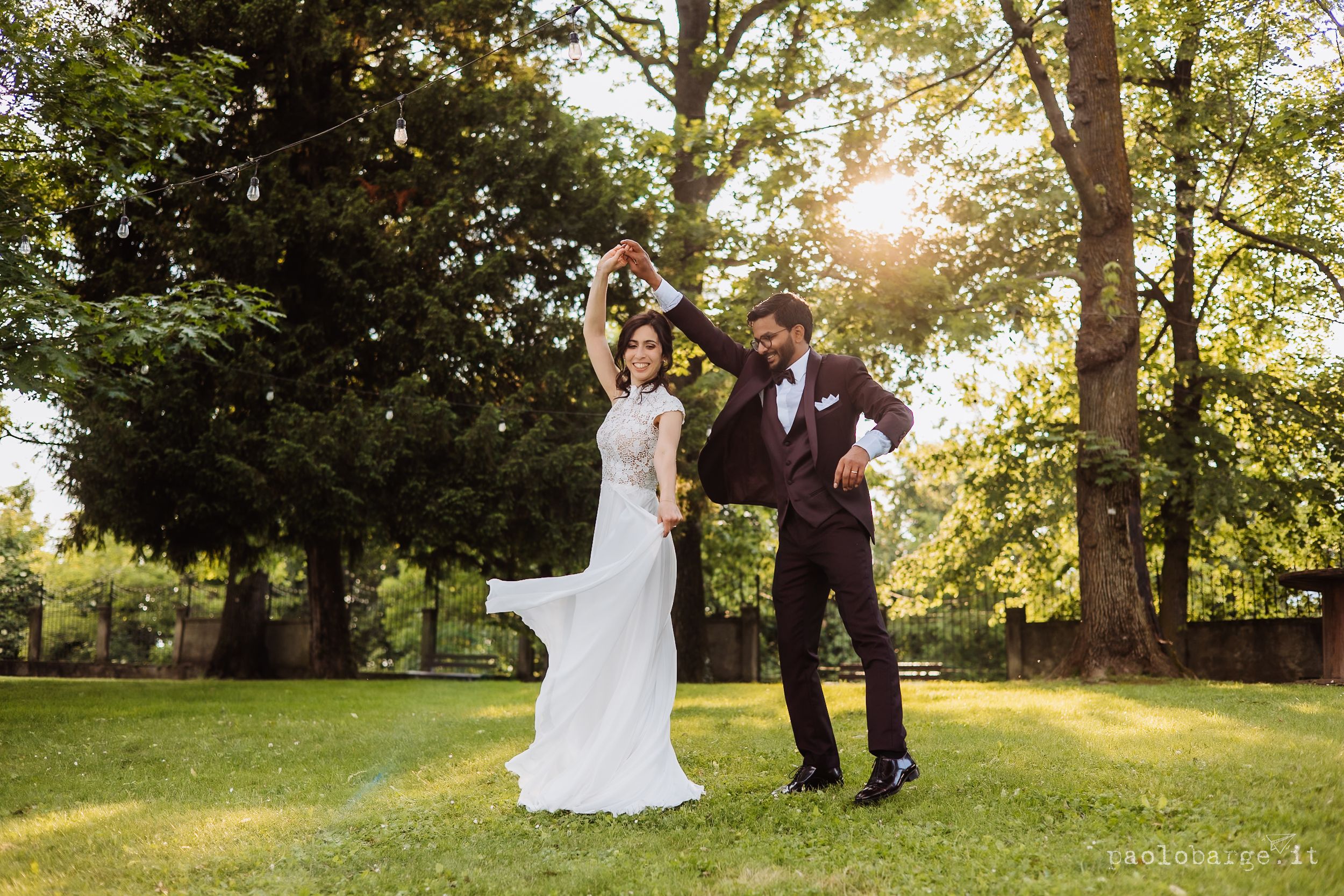 Newlywed couple poses together in golden sunlight filtering through trees in a lush garden setting.