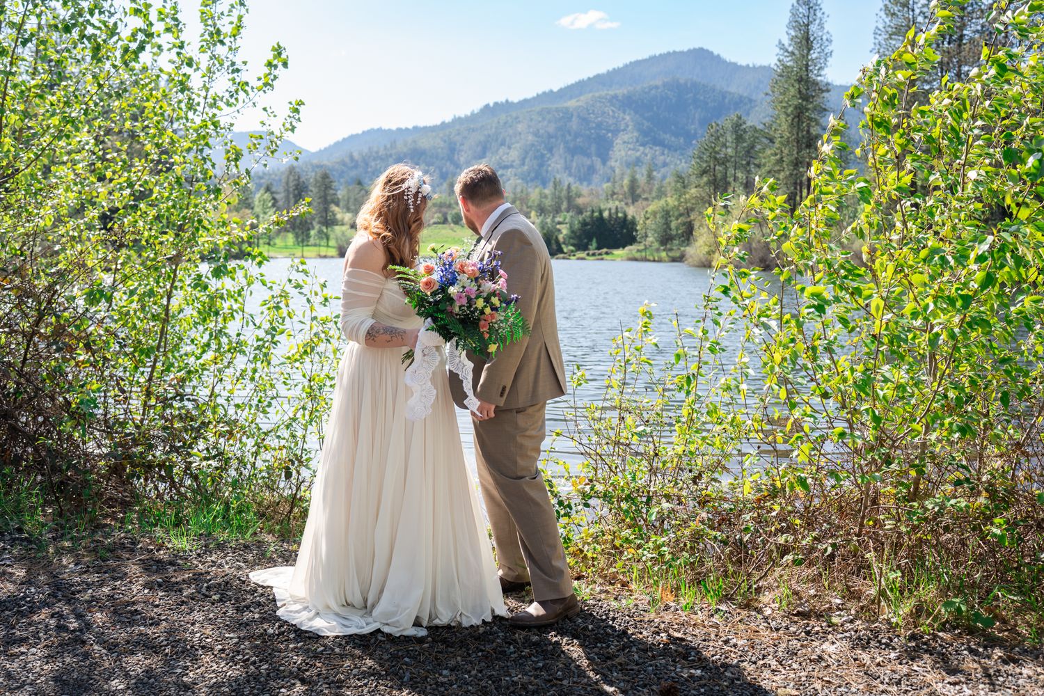portrait of the bride and groom looking out over the pond at Pacifica Gardens in Southern Oregon with the mountains in the background