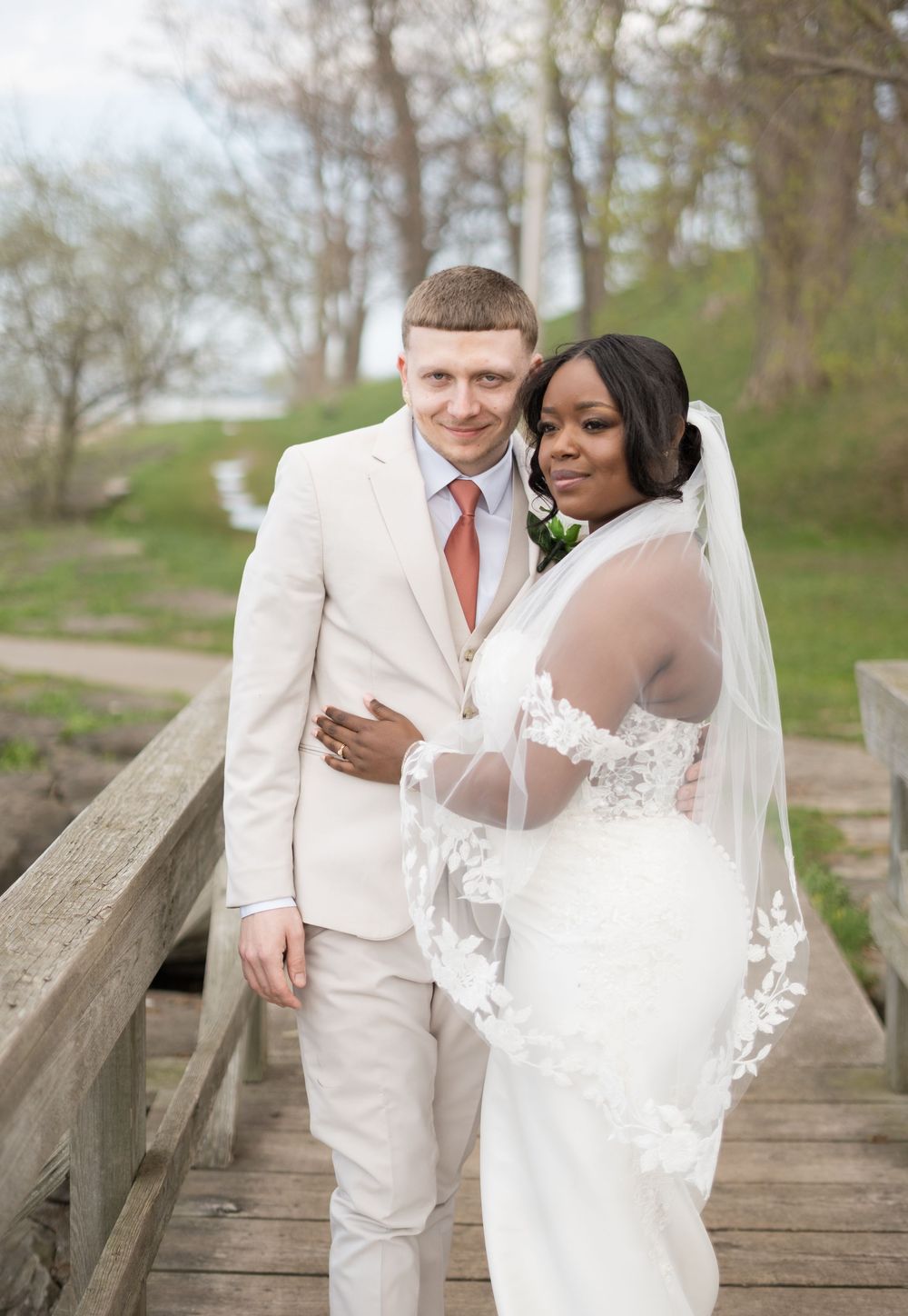 A bride and groom pose together on a wooden bridge during their spring wedding ceremony.