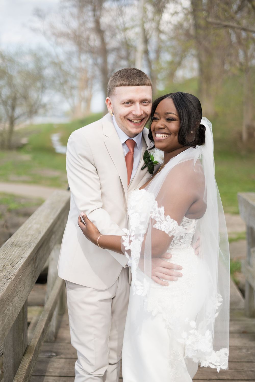A romantic wedding couple sharing tender moments on a rustic wooden bridge in a spring garden setting.