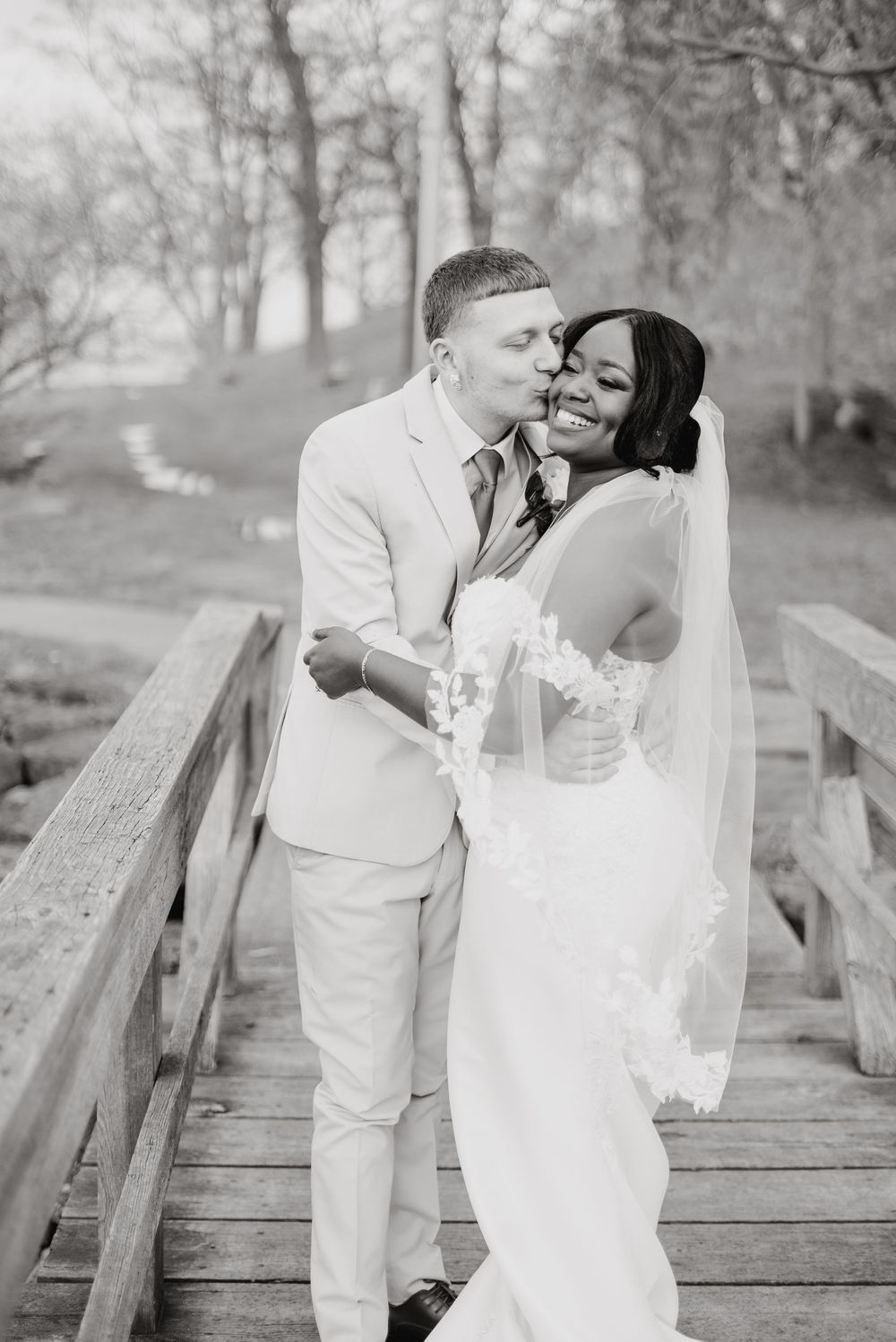 A happy couple shares a romantic moment on a wooden bridge in black and white wedding photography.