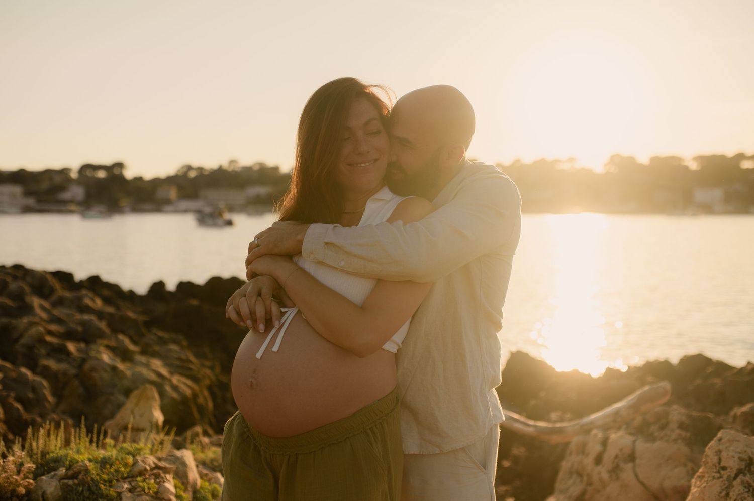 Photo d'une femme enceinte au coucher du soleil au bord de mer enlacée par son mari