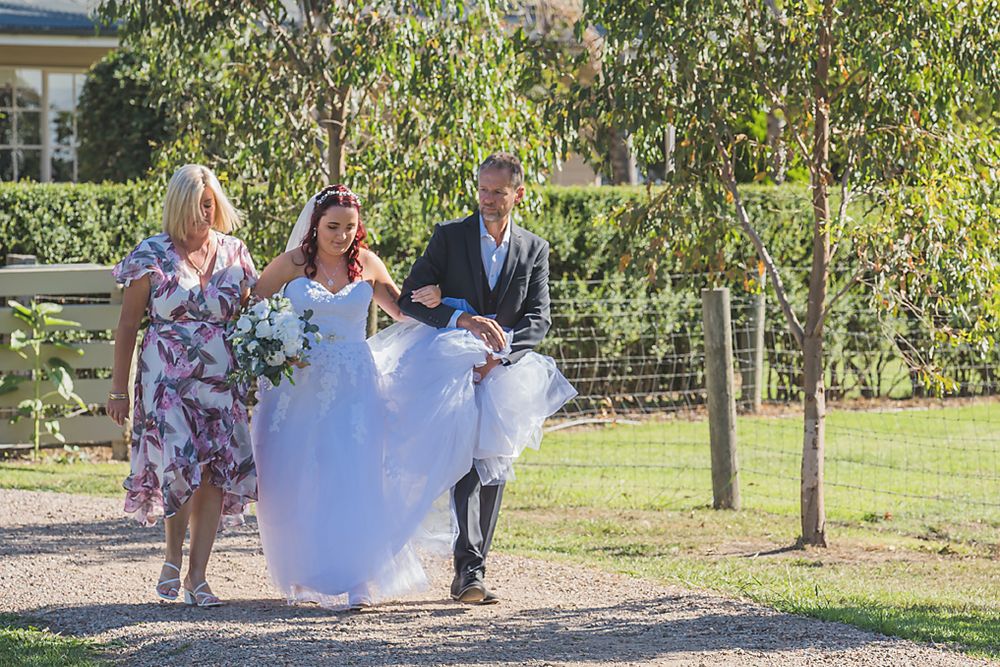 Group wearing formal attire running playfully through a garden path on a sunny afternoon.