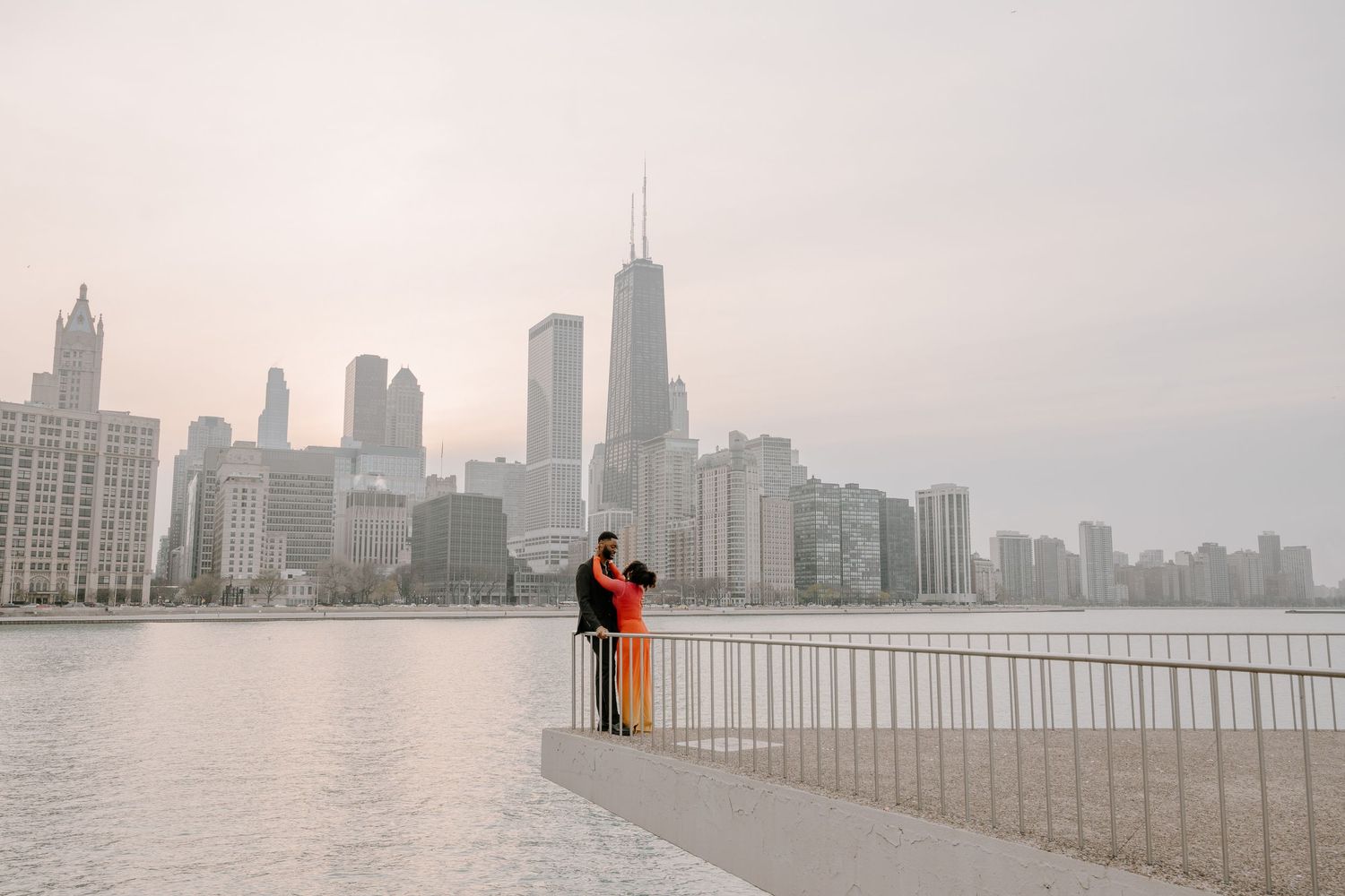 A couple embraces on the Chicago lakefront with the city skyline and Lake Michigan in the misty background.