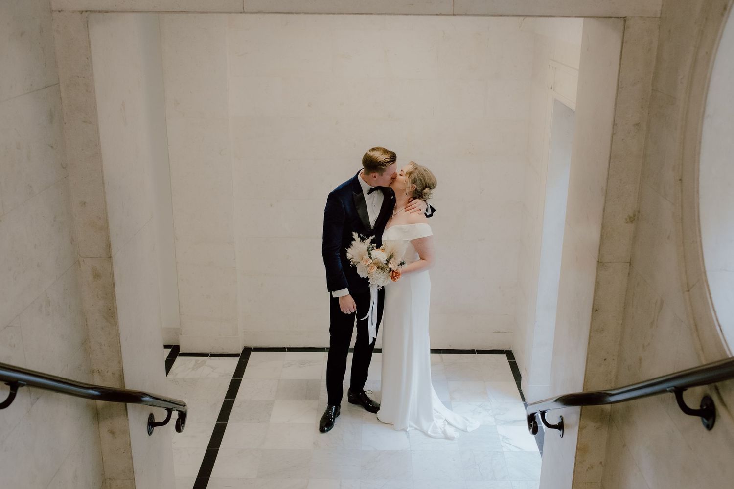 A bride and groom share an intimate moment while standing at the top of a white marble staircase.