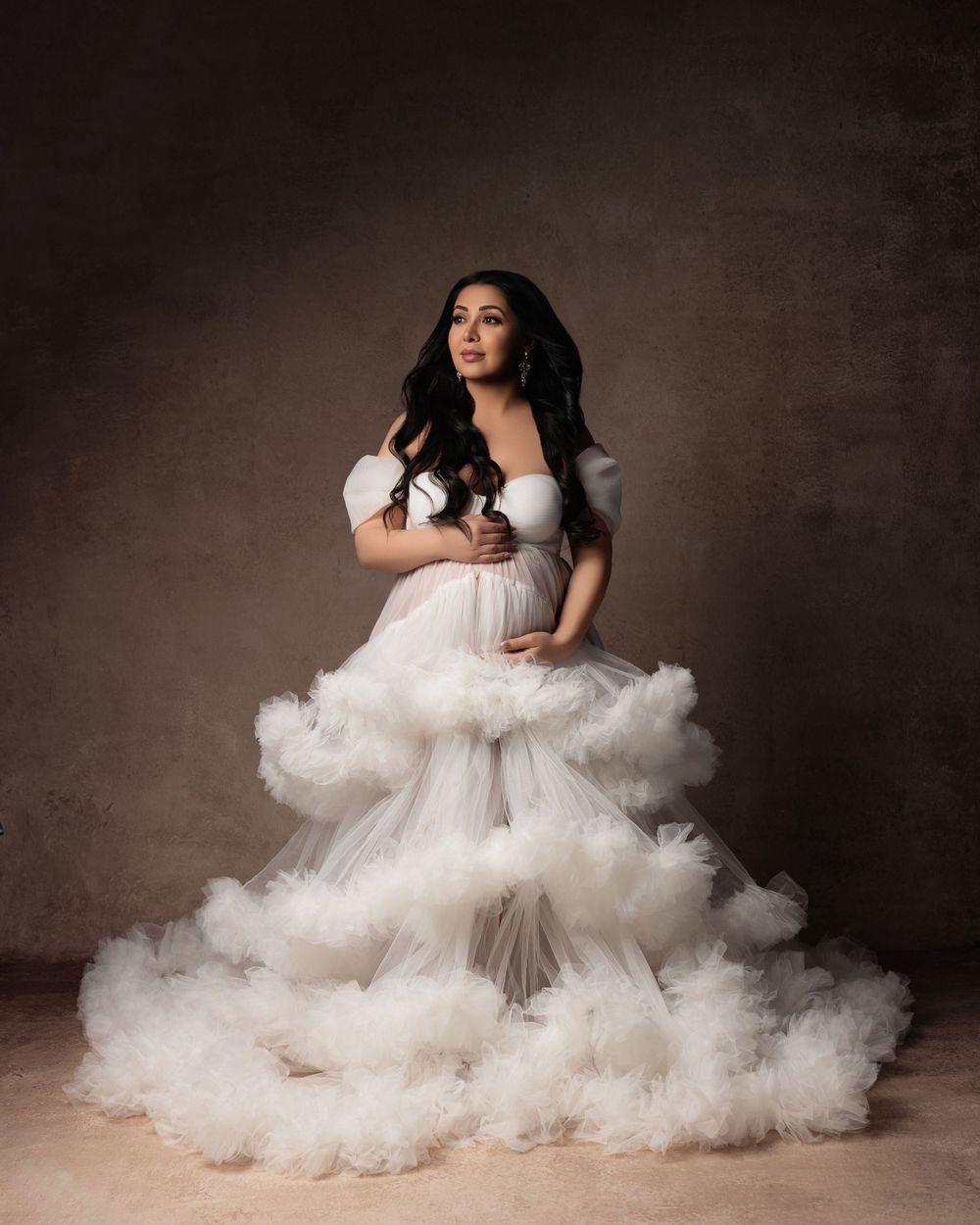 A dramatic portrait of someone wearing an ethereal white ballgown with cascading tulle layers against a dark backdrop.