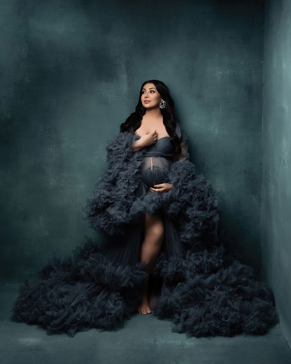 Artistic maternity portrait in teal tones featuring a dramatic billowing smoky tulle gown against textured backdrop.