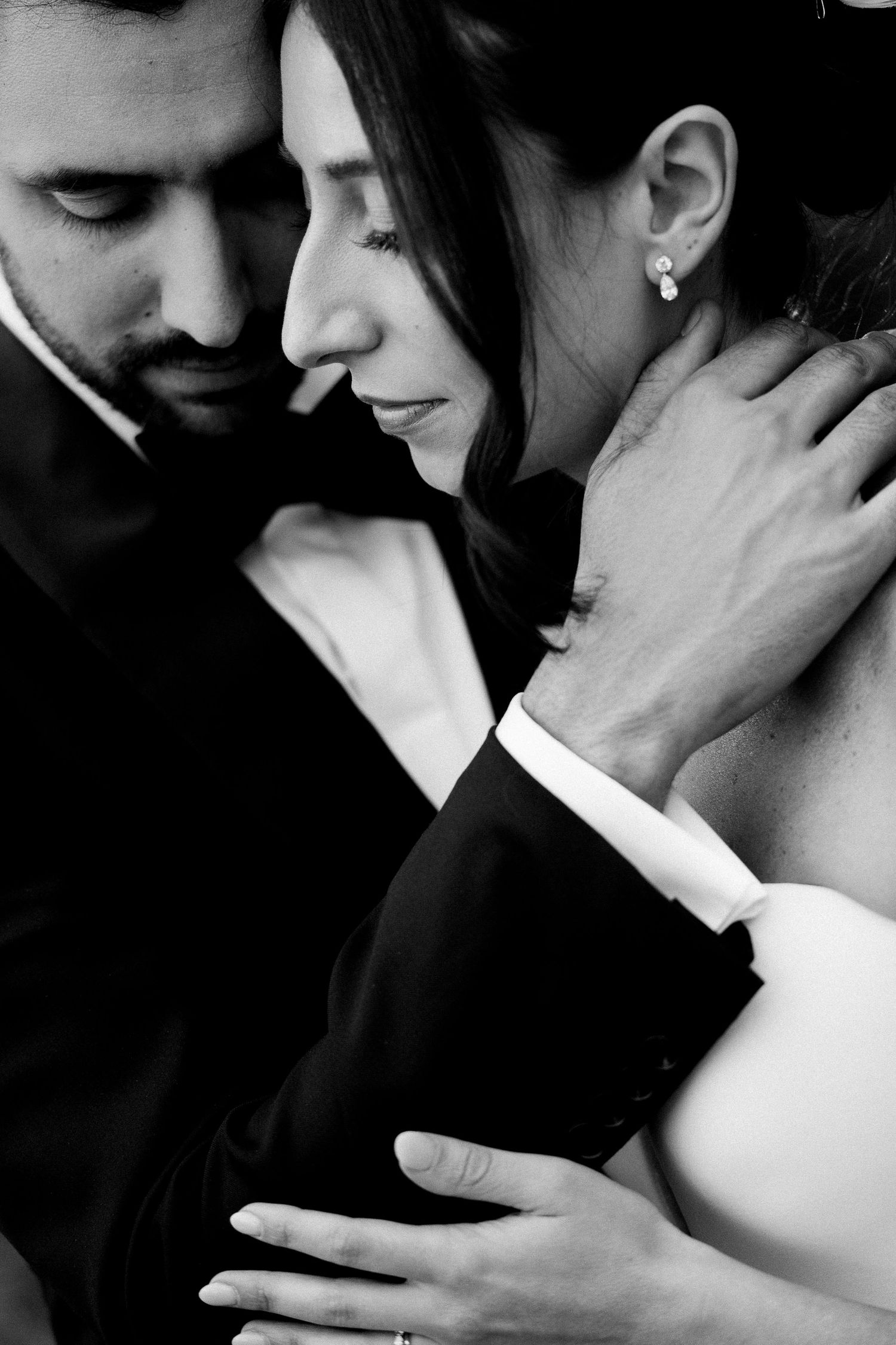 Tender black and white portrait of couple embracing intimately in formal attire with soft lighting.