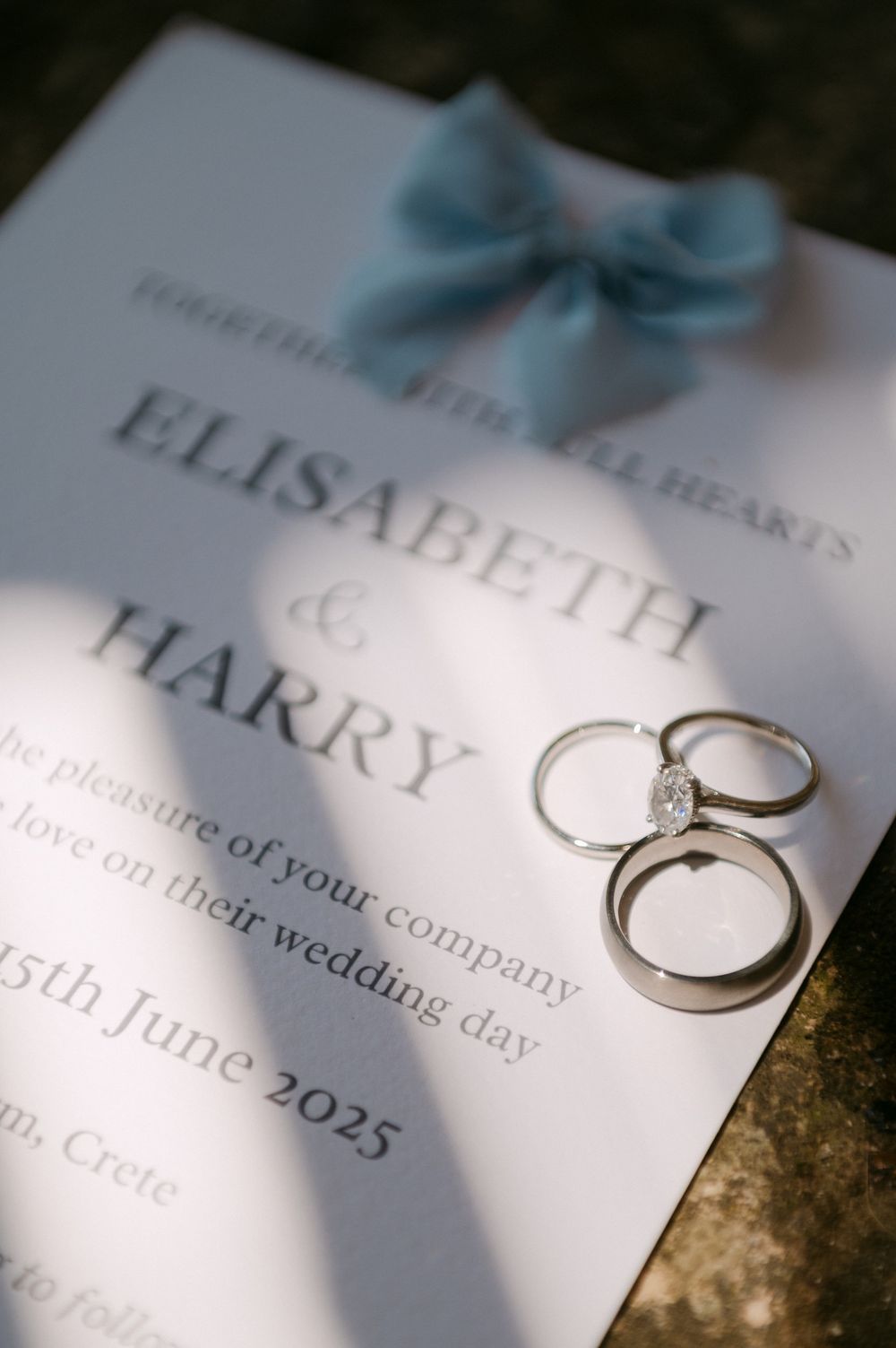 Wedding rings cast shadows on wedding invitation cards showing details of the ceremony date and names.