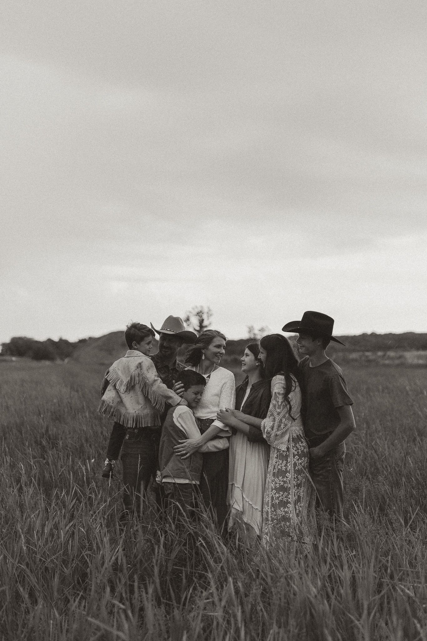 A vintage black and white photograph shows a group of people walking through a tall grain field in rural countryside.