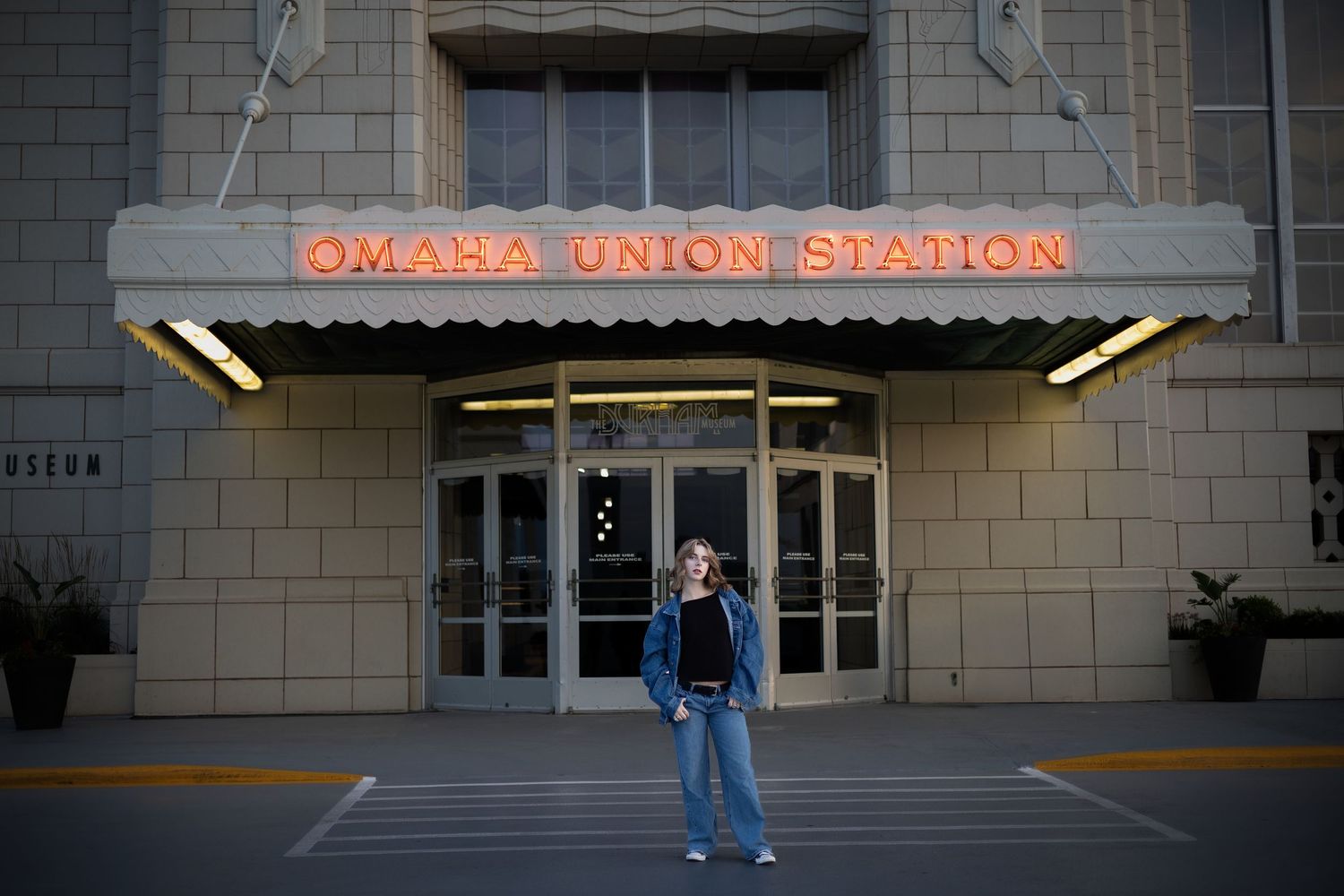 Someone stands in front of the entrance to Omaha Union Station at dusk with illuminated signage above the doorway.