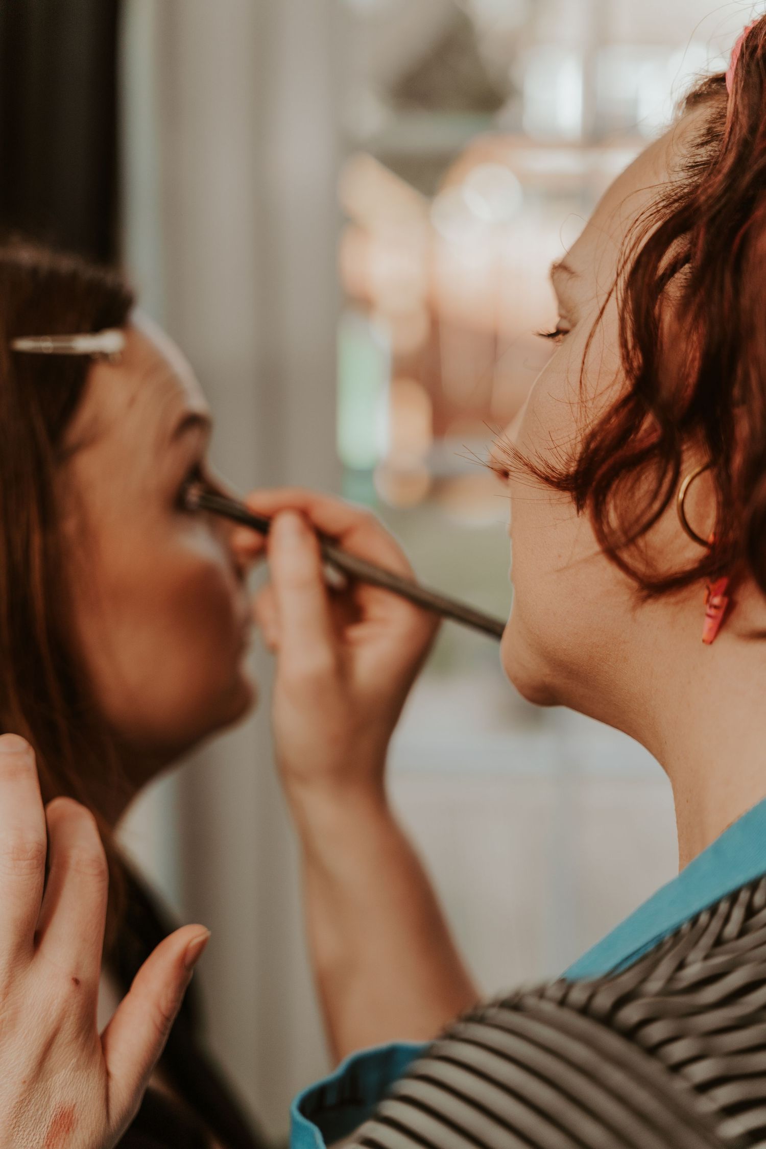 Close up shot of a makeup artist applying eye makeup to a client in natural lighting.