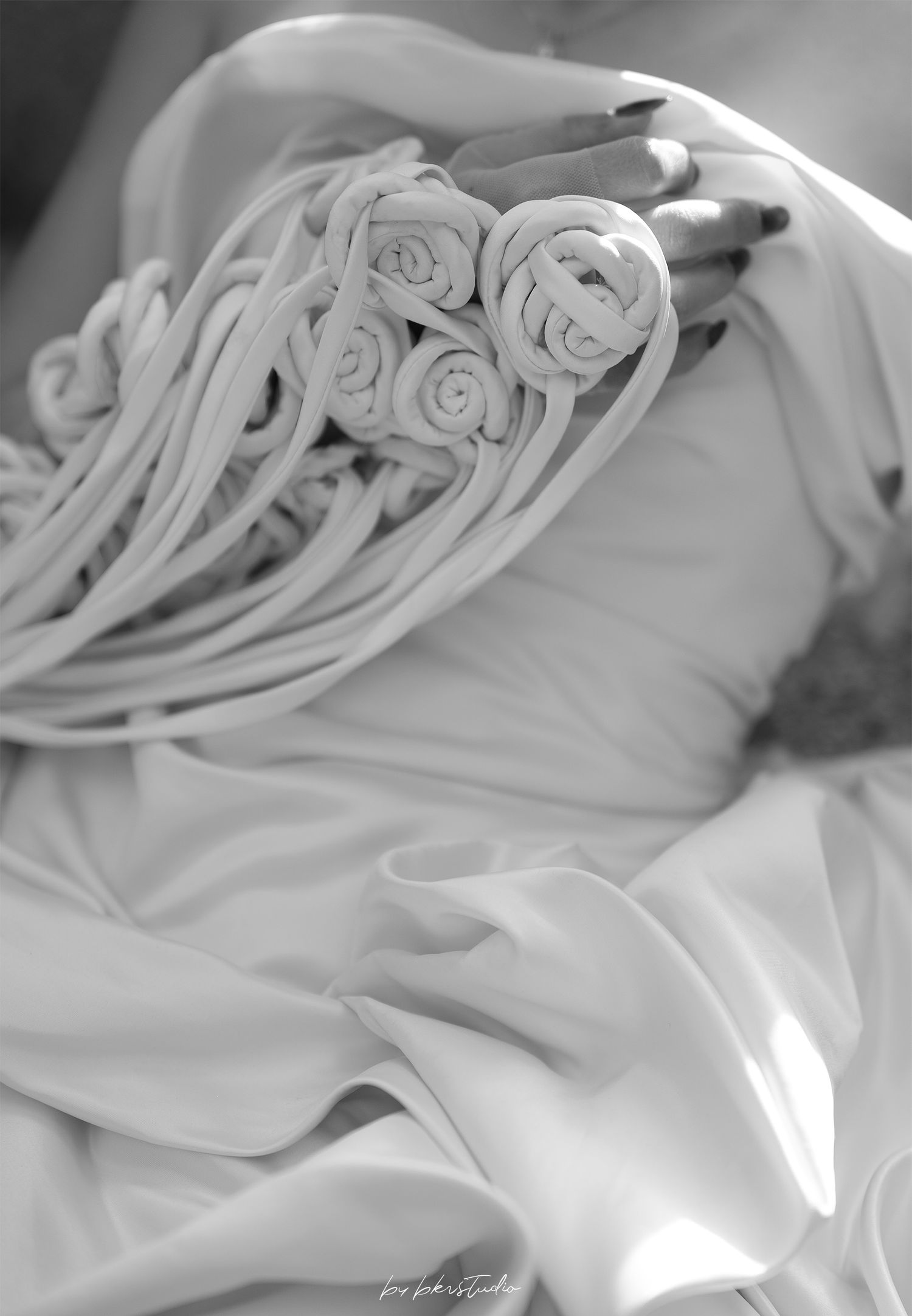 Close-up black and white photograph of delicate fabric draping with rose-like pleating details.