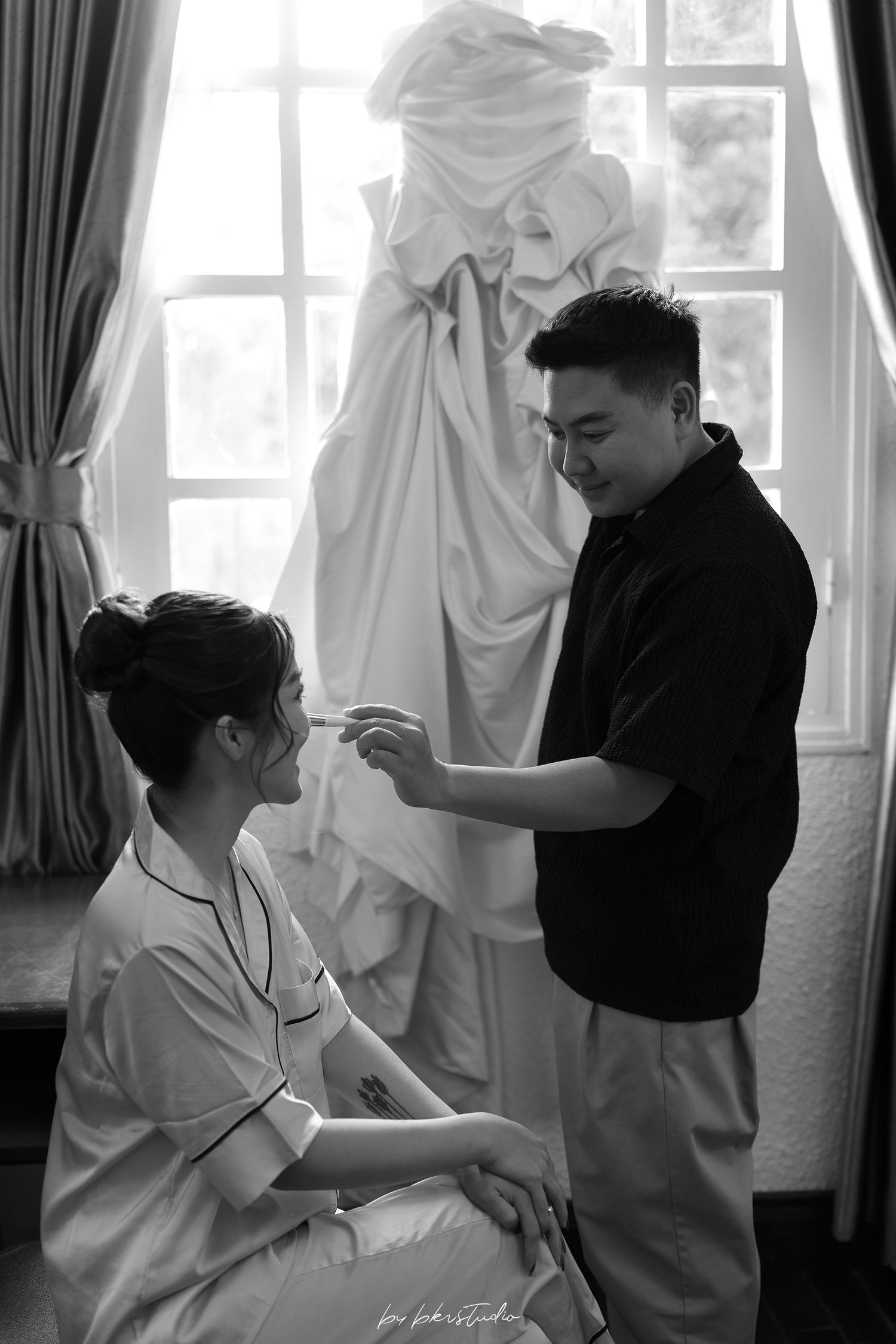 A black and white photo shows preparation before a wedding ceremony with a flowing white dress visible in background.