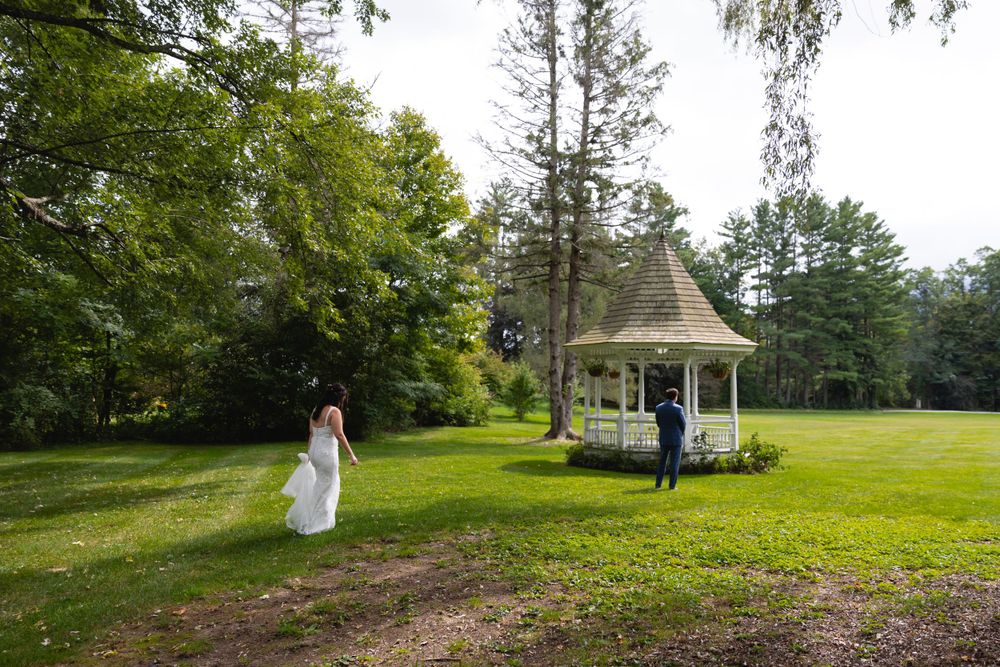 A romantic moment captured at a white gazebo in a lush green garden setting during a wedding ceremony.