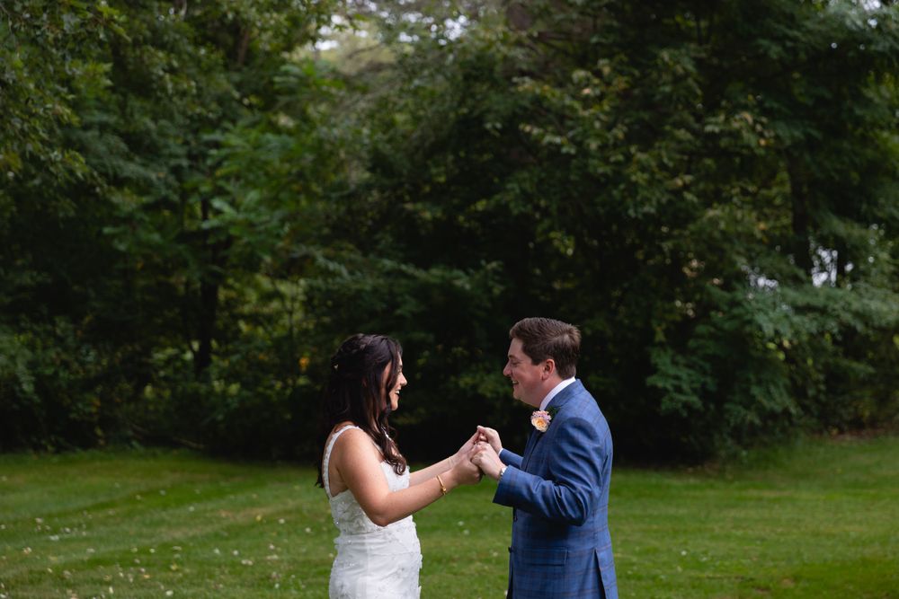 A couple dances and smiles together on a lush green lawn with trees in the background.
