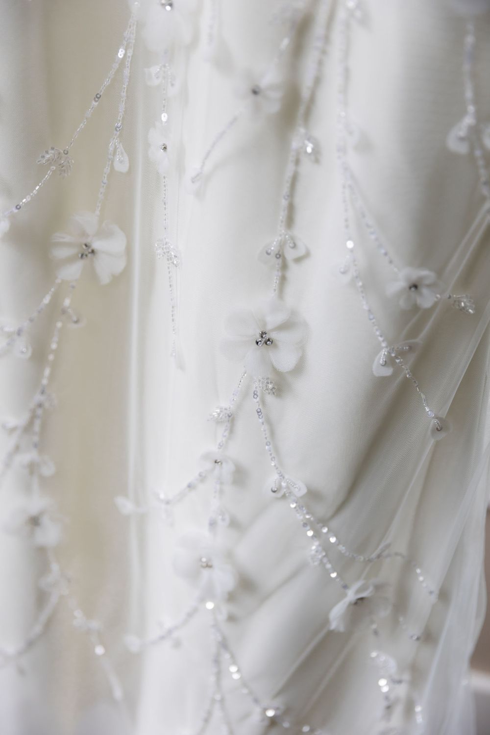 Delicate white beaded details and embroidery on flowing wedding dress fabric create an ethereal texture.