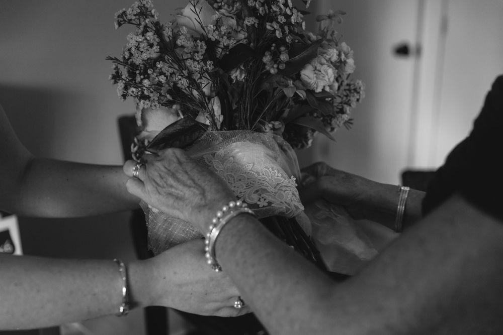 Black and white close-up image of hands wearing bracelets arranging flowers in a vase.