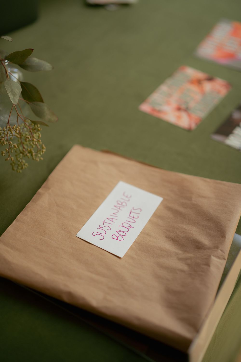 A brown paper wrapped package with 'Something Better' label sits on a green surface next to blurred cards and flowers.
