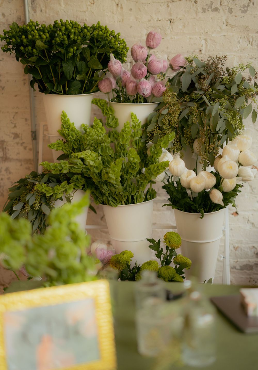 Fresh flower arrangements in white vases featuring pink tulips and greenery against a white brick wall.