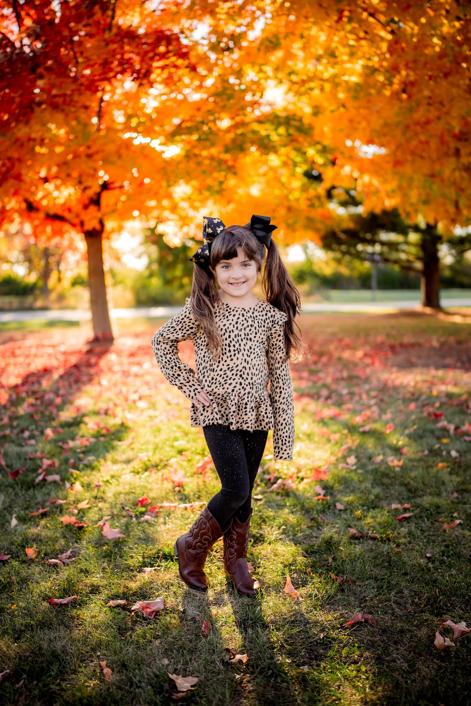 A leopard print sweater and boots create a stylish autumn outfit against vibrant fall foliage in a park setting.