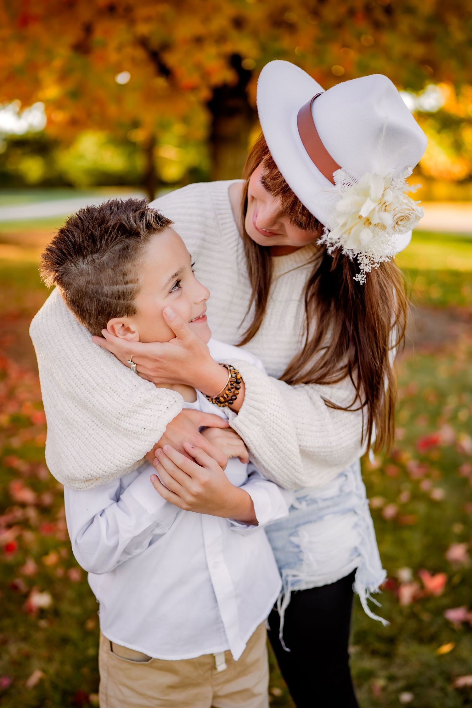 A tender embrace between two people wearing white sweaters in an autumn park with colorful fall foliage in the background.