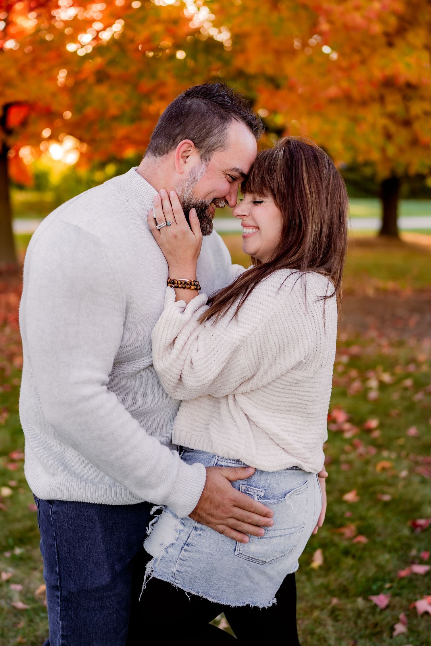A romantic couple embraces outdoors during autumn with vibrant orange fall foliage in the background.