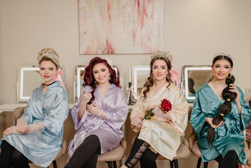 Four people in colorful satin robes sit elegantly in vintage-style chairs against a cream wall with pink artwork.