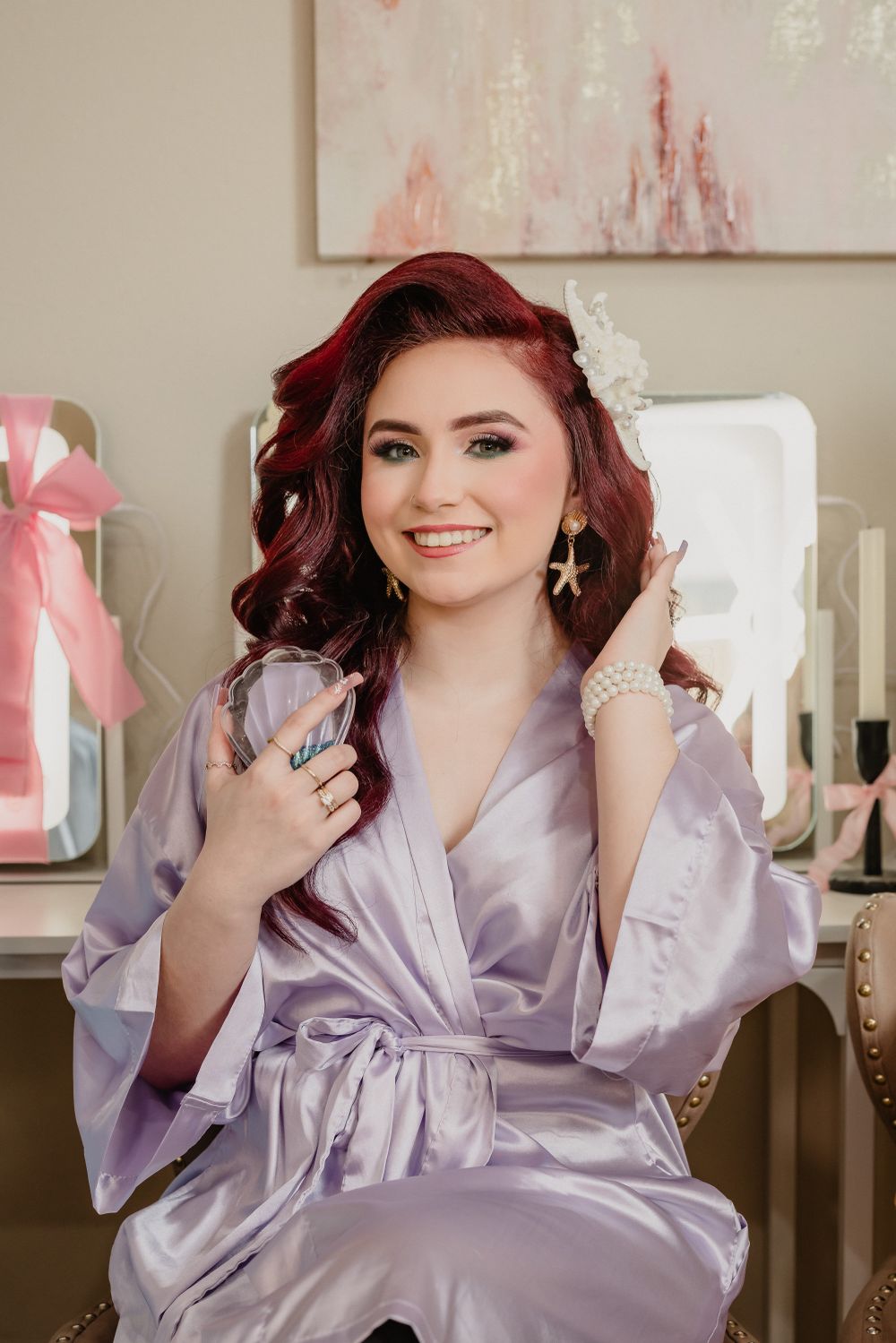 Person wearing a lavender silk robe poses elegantly in a boudoir setting with pink decor.