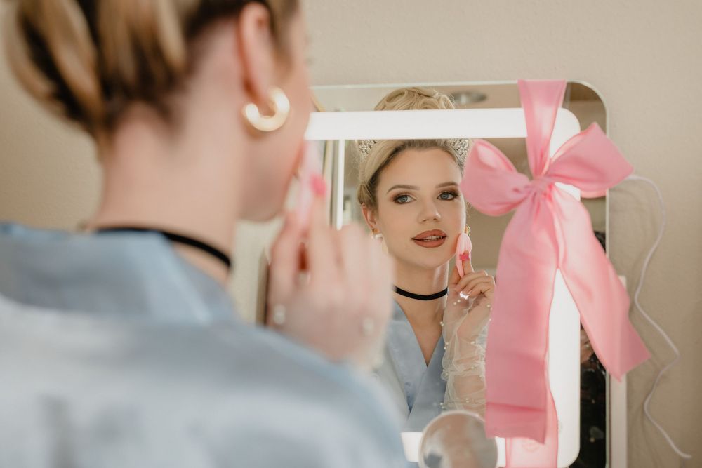 Someone looks in a mirror decorated with a pink bow while getting ready at home.