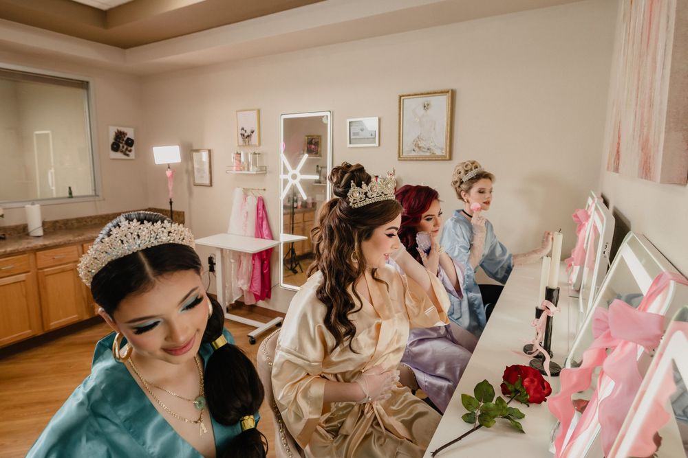 People in satin robes gather at a makeup counter in a bridal preparation room with pink decorative elements.