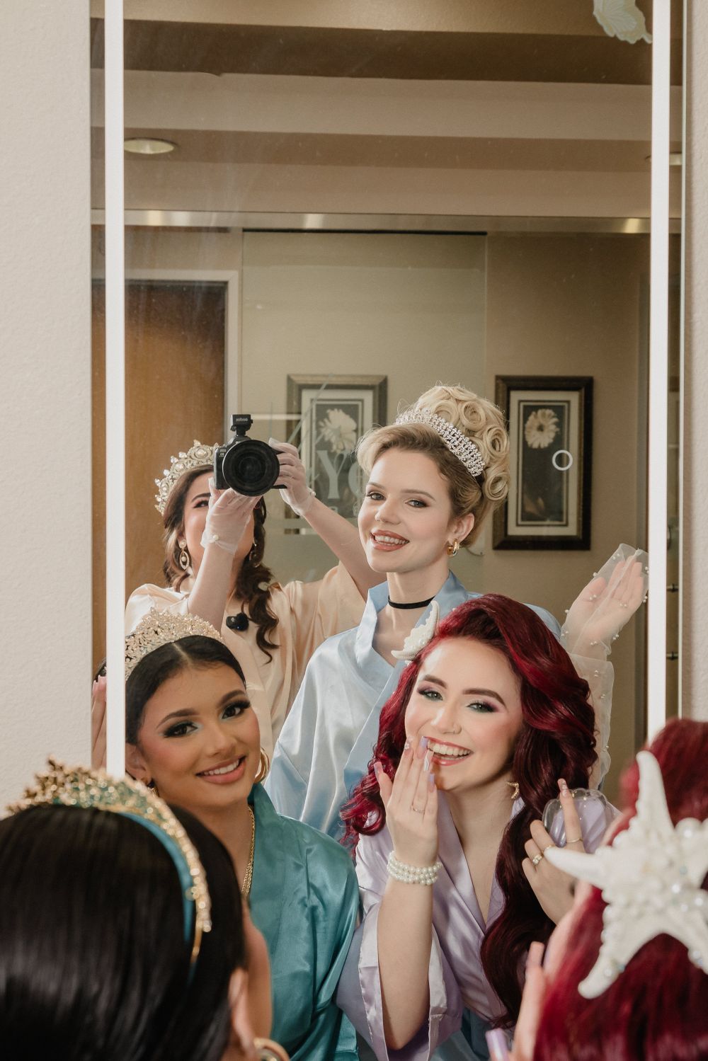 A group wearing fancy dresses, tiaras and formal attire poses together in an indoor setting.