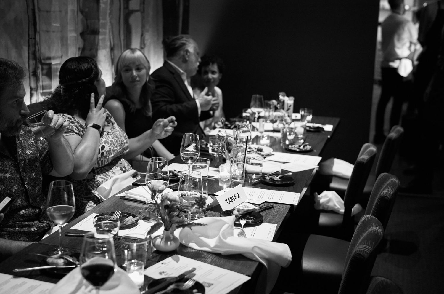 Elegant black and white photograph of a formal dinner party with wine glasses and place settings at a long table.