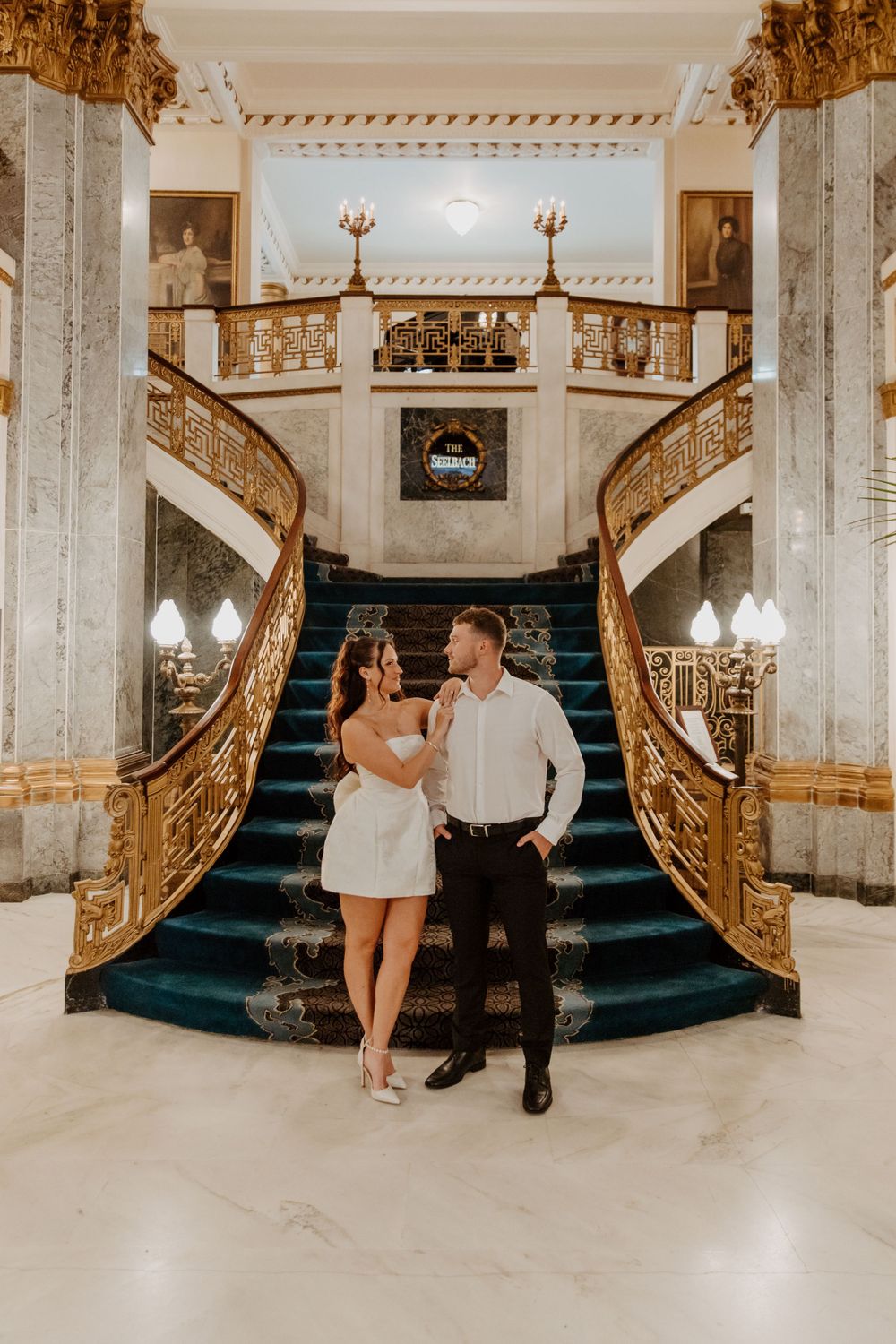 Couple posing on an elegant marble staircase with ornate gold railings in a luxurious interior at the Seelbach Hotel in Louisville, Kentucky
