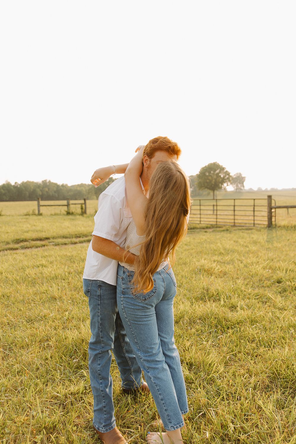 Couple embracing in field with wooden fence and golden sunlight in Lexington, Kentucky.