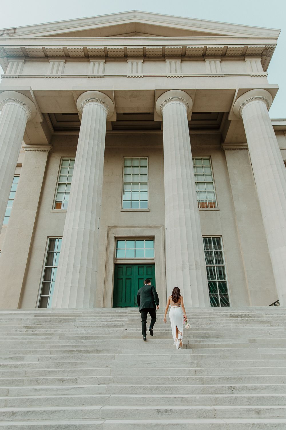 Couple ascending stairs of a neoclassical building with massive white columns in Louisville, Kentucky.