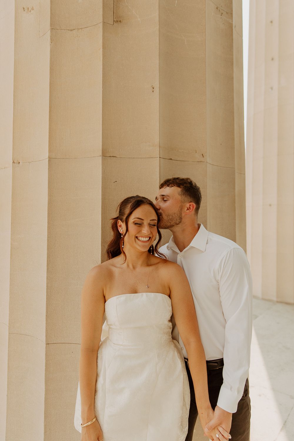 Couple embraces between elegant stone columns in an intimate wedding portrait with warm lighting in Louisville, Kentucky.