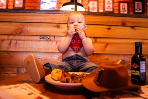 A young child in western wear sitting at a wooden restaurant booth with dinner.
