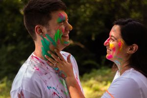 Couple with painted faces gaze at each other while covered in vibrant Holi colors.