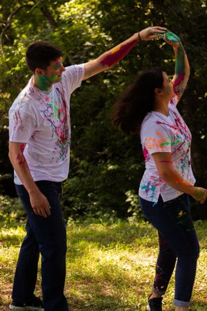 Couple in white shirts covered in powder paint dance together in a sunny garden.