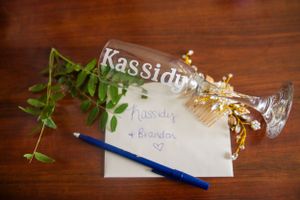 Personalized champagne glass with greenery and a handwritten note on white paper.