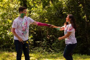 Couple in powder-stained white shirts hold hands while dancing in a sunlit outdoor setting.