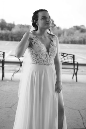 Elegant wedding dress with plunging lace neckline and flowy skirt photographed in black and white against outdoor setting.