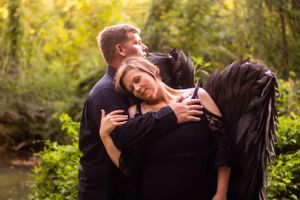 Couple in black clothing share an intimate moment in a golden-lit forest setting.