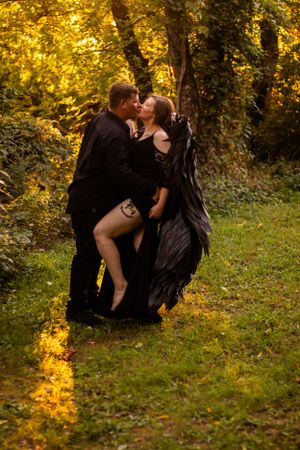 Romantic couple in dark clothing embrace among autumn trees with dramatic lighting.