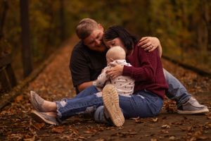 Family sits together on autumn forest floor with small child.