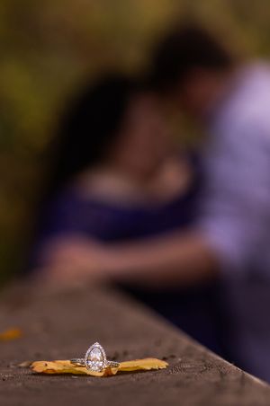 A sparkling engagement ring sits on a wooden surface with a blurred background.