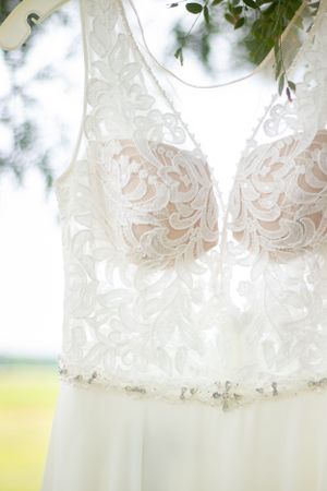 Close-up detail of a white lace wedding dress bodice hanging against a soft blurred background.