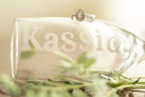 Close-up of etched glassware with 'Kassidy' text and decorative foliage.