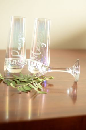 Two personalized champagne flutes with decorative text lying on a wooden surface.